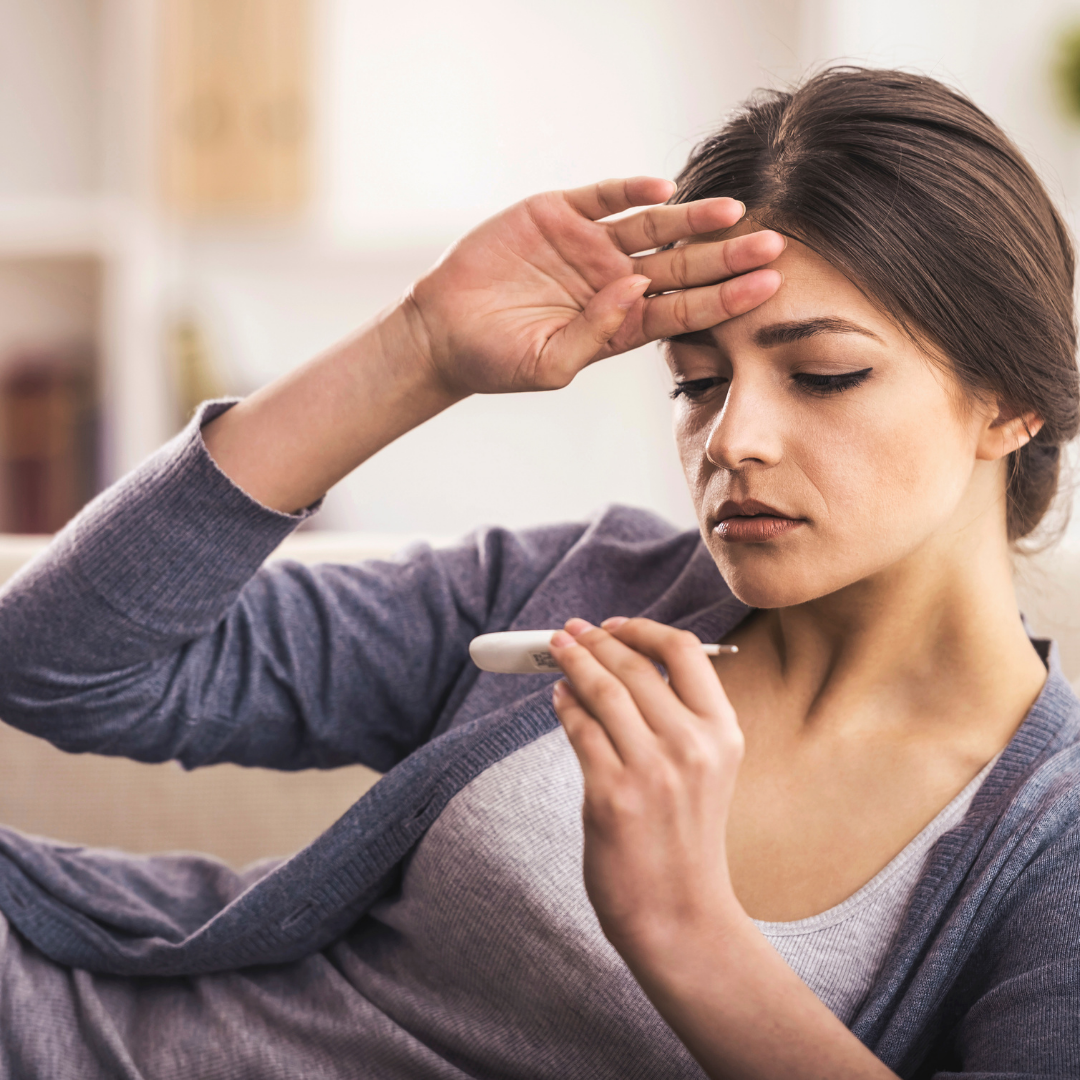 Young lady on couch with hand on her forehead while looking at a thermometor