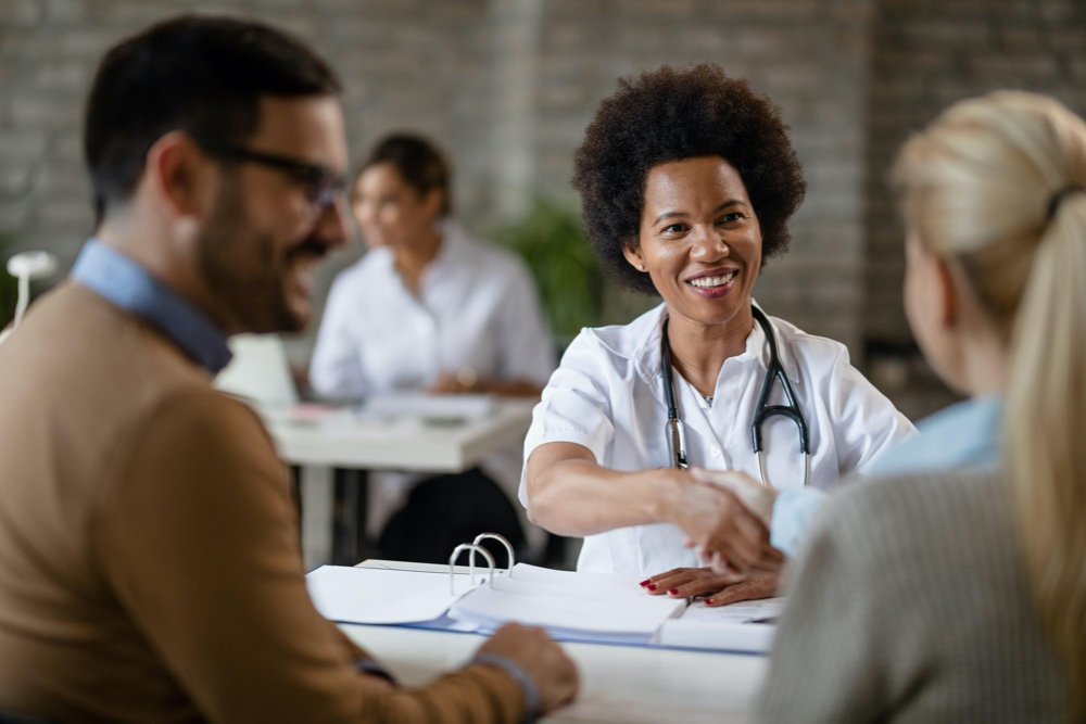 Happy african american doctor shaking hands with a couple after medical appointment at clinic
