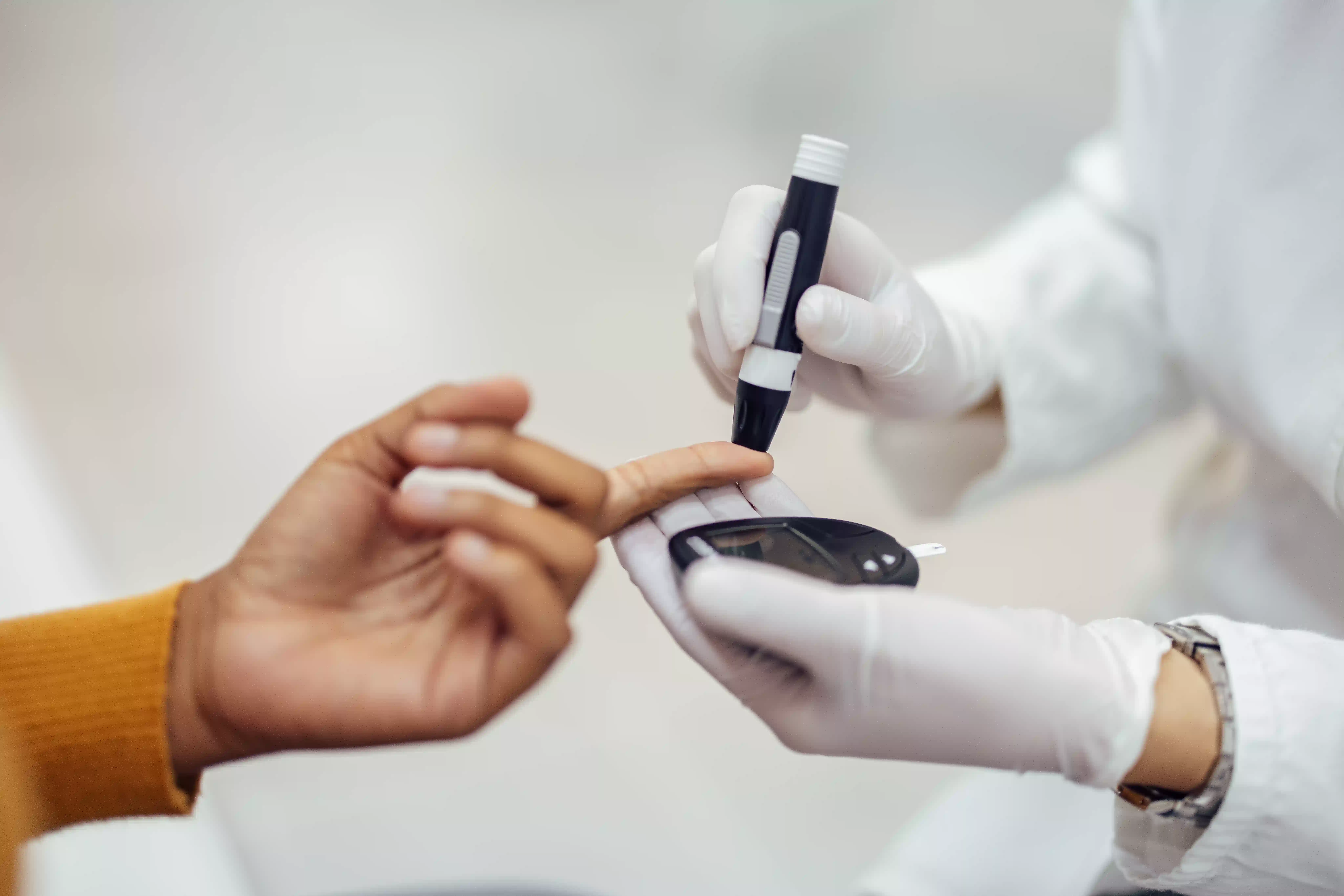 Healthcare professional using a lancing device on a patient's finger for diabetes blood testing, with a blood glucose meter visible.